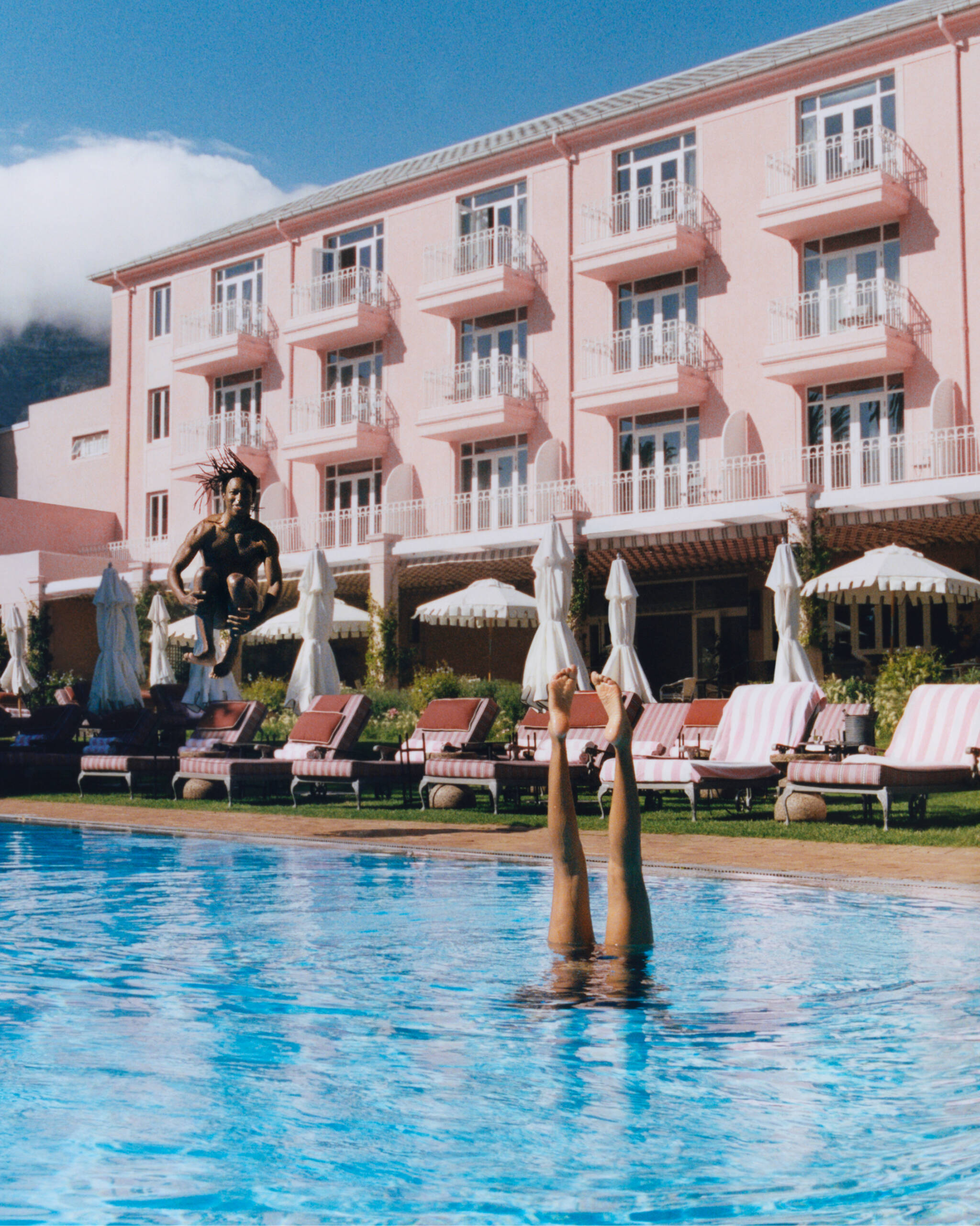 Pool with woman doing handstand with pink building behind