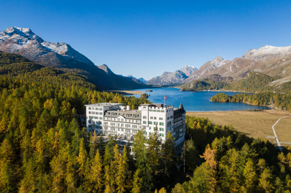 white building in the middle of a forest with lake behind