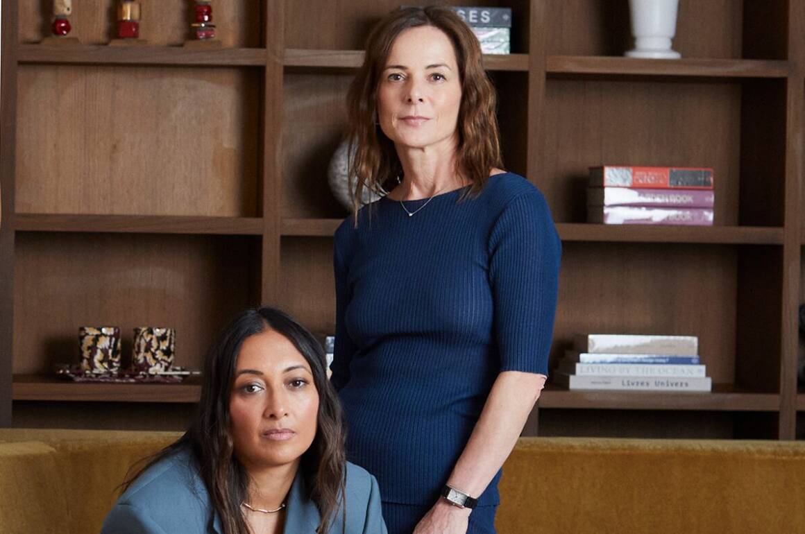 two women, one sitting one standing, wearing blue with a brown background