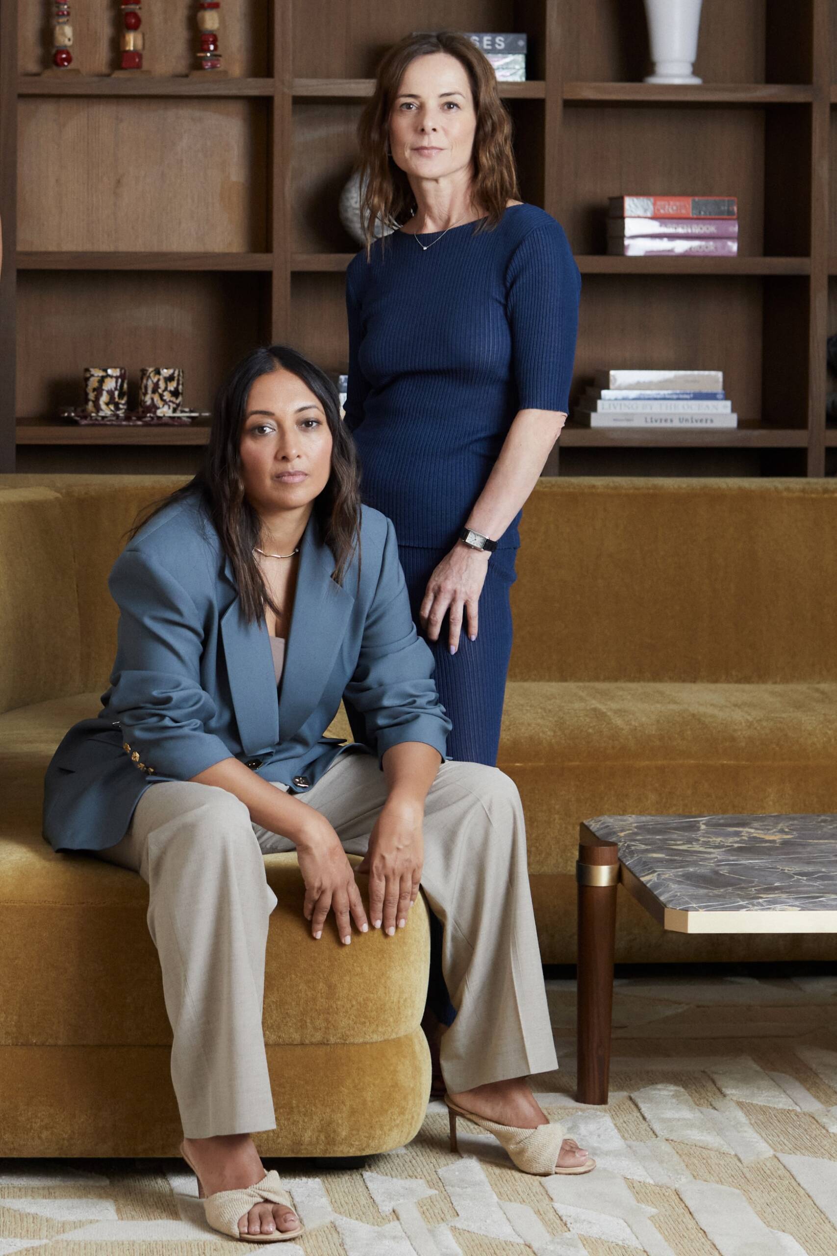 two women, one sitting one standing, in a sitting room, with colours of yellow and blue